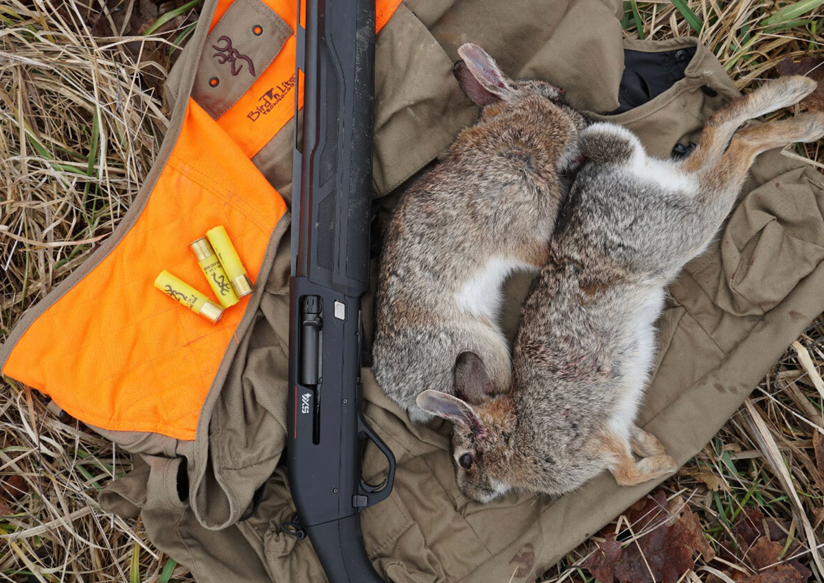 One of the best guns for rabbit hunting laying on a vest with shells and harvested rabbits.