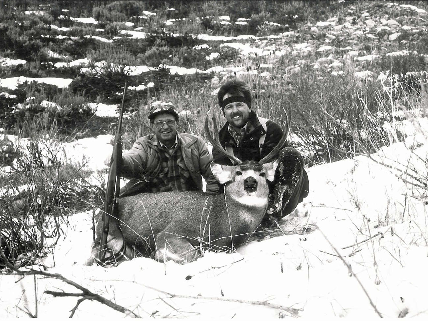two hunters kneeling behind buck in snow