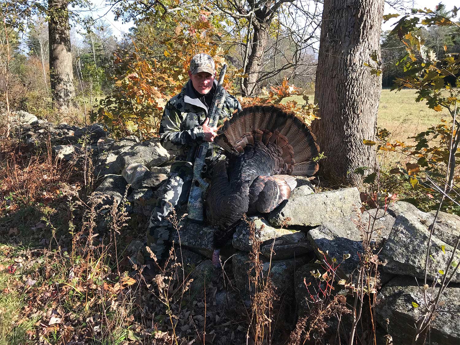 hunter posing with a turkey on a stone wall