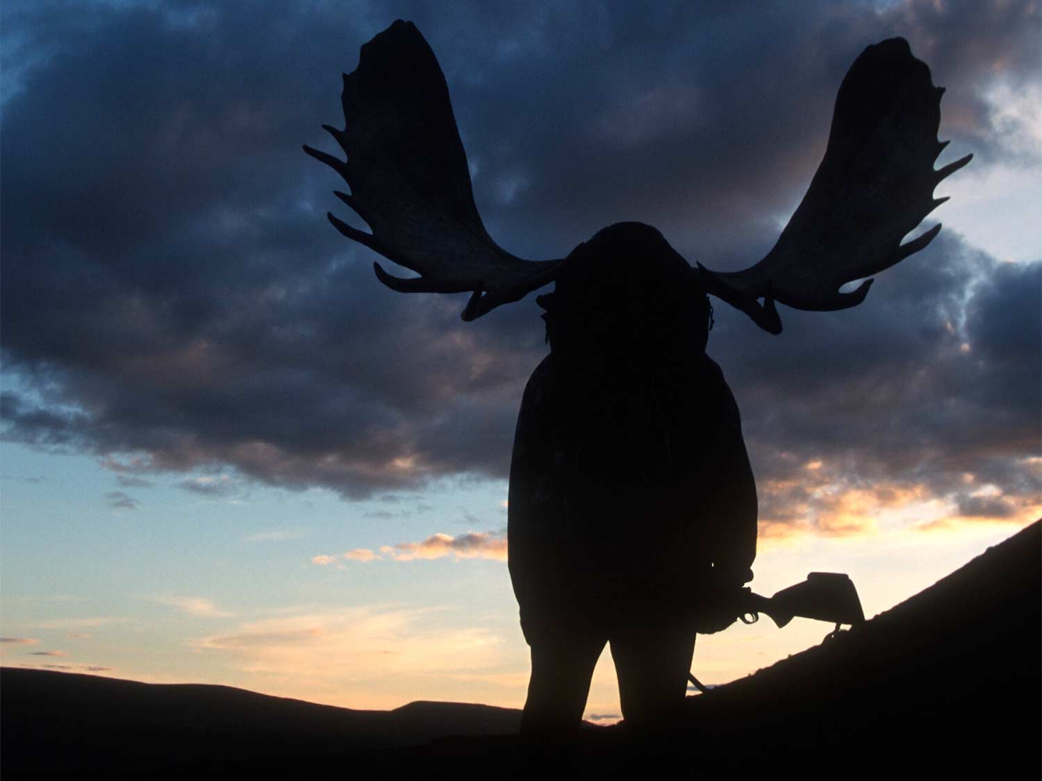 silhouette of a hunter shouldering moose antlers