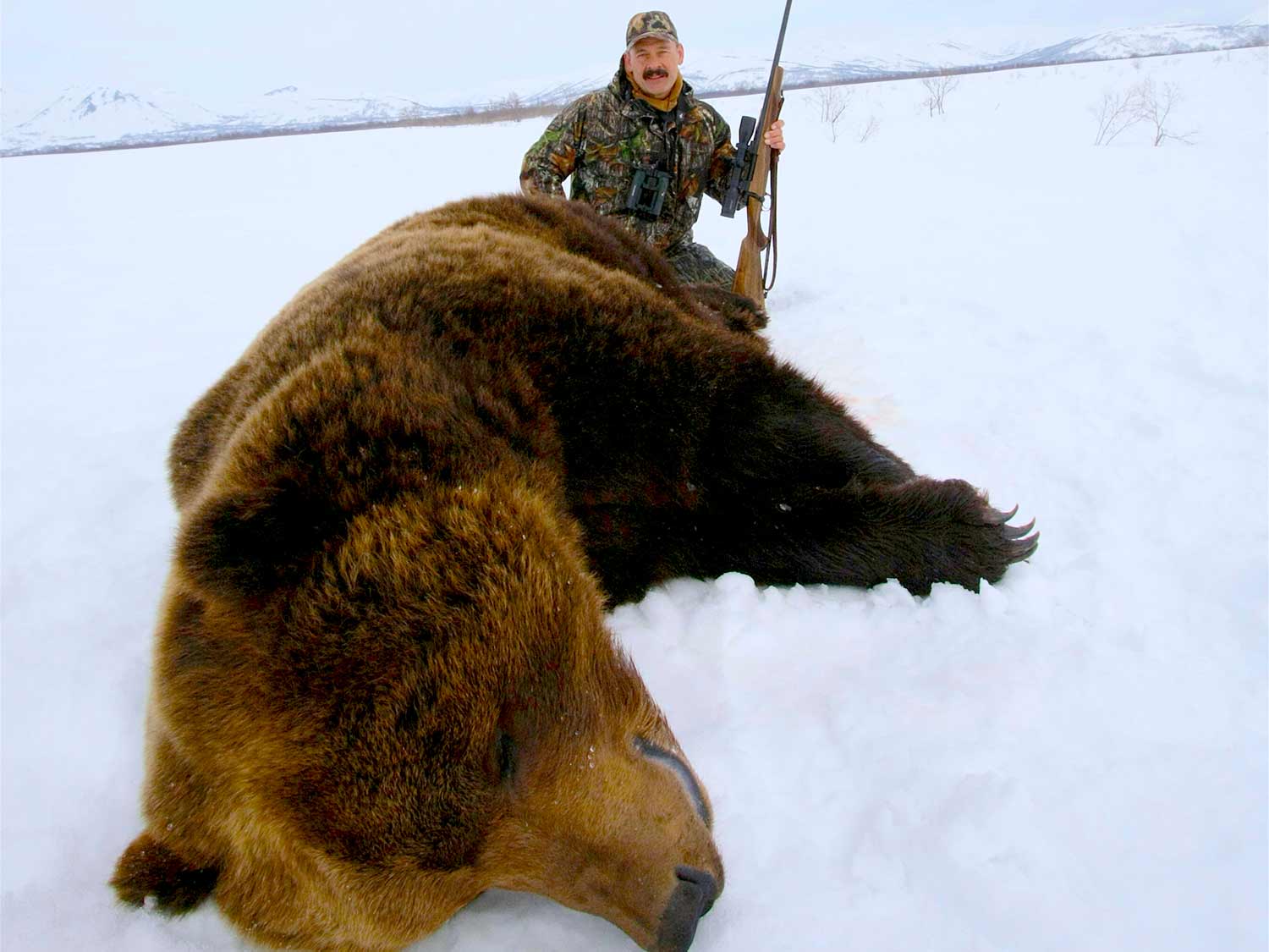hunter kneeling behind brown bear in the snow
