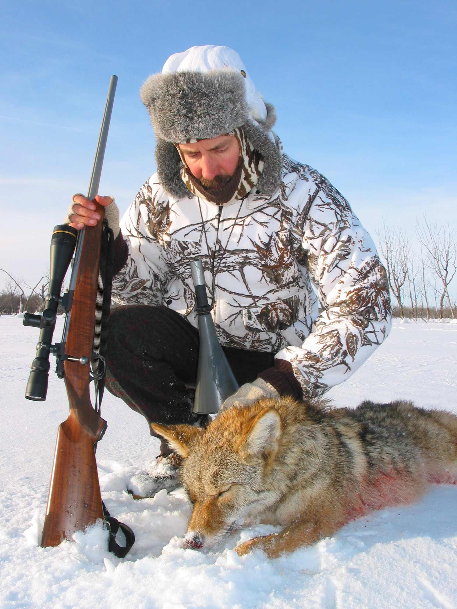 hunter kneeling next to a coyote in the snow