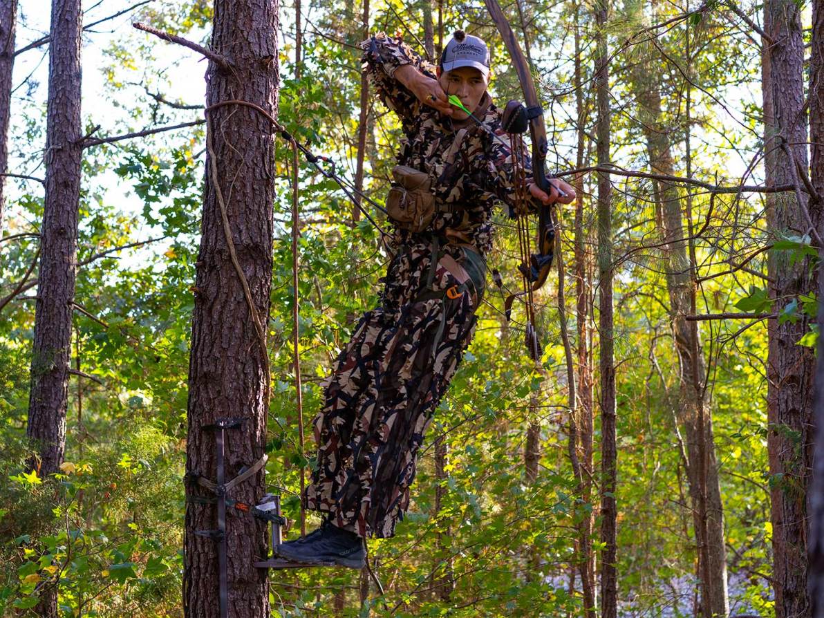 hunter shooting a bow and arrow from a tree saddle stand