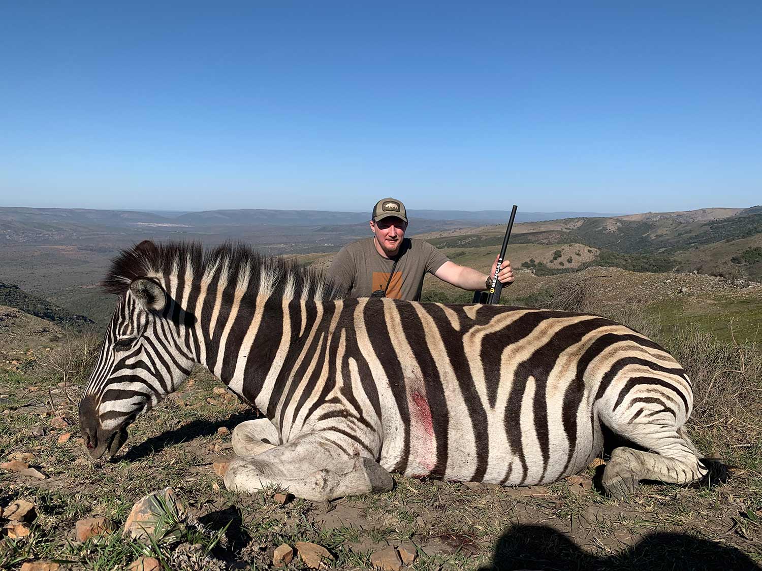 A hunter kneeling behind a zebra on an African hunting trip.