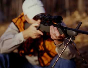 A hunter aiming a rifle using shooting sticks.