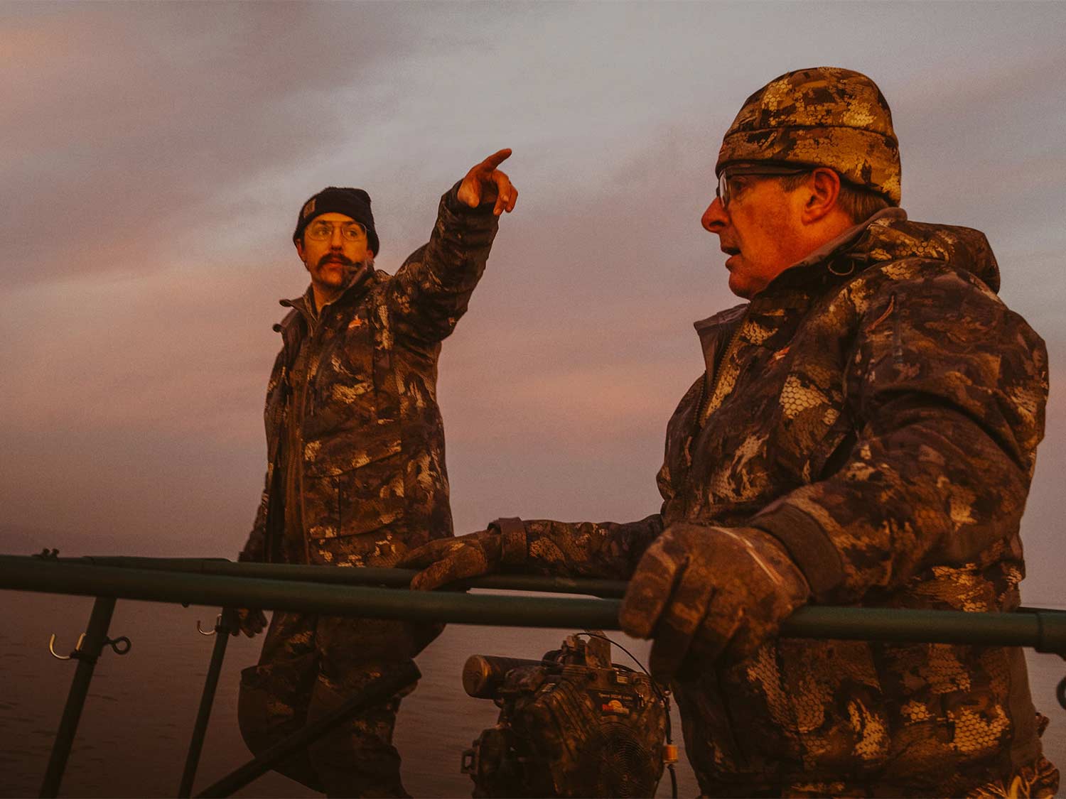 Two male hunters in a field at sunset.