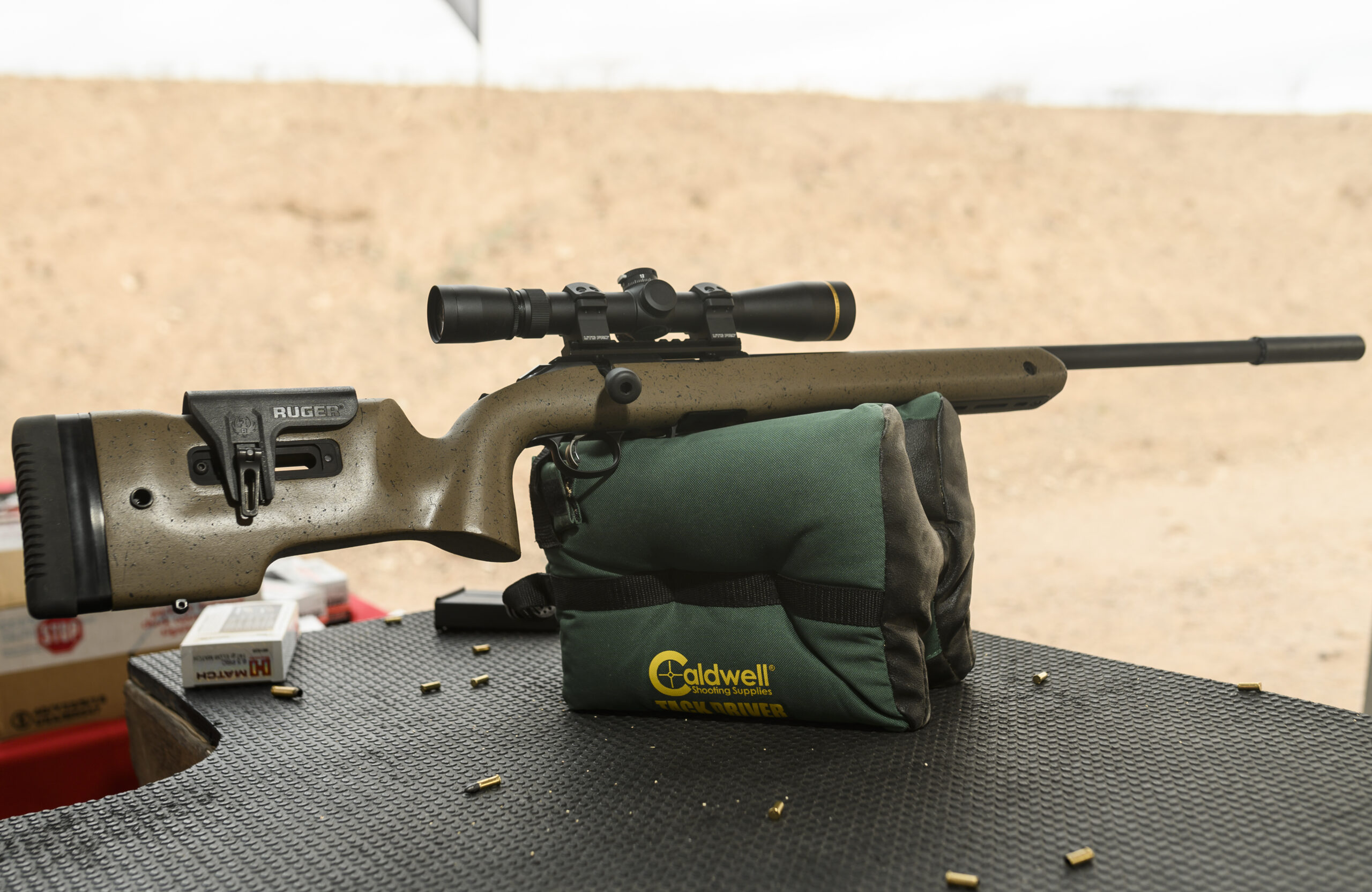 a rimfire rifle resting on a shooting bag at the range with empty 22 shells on the table