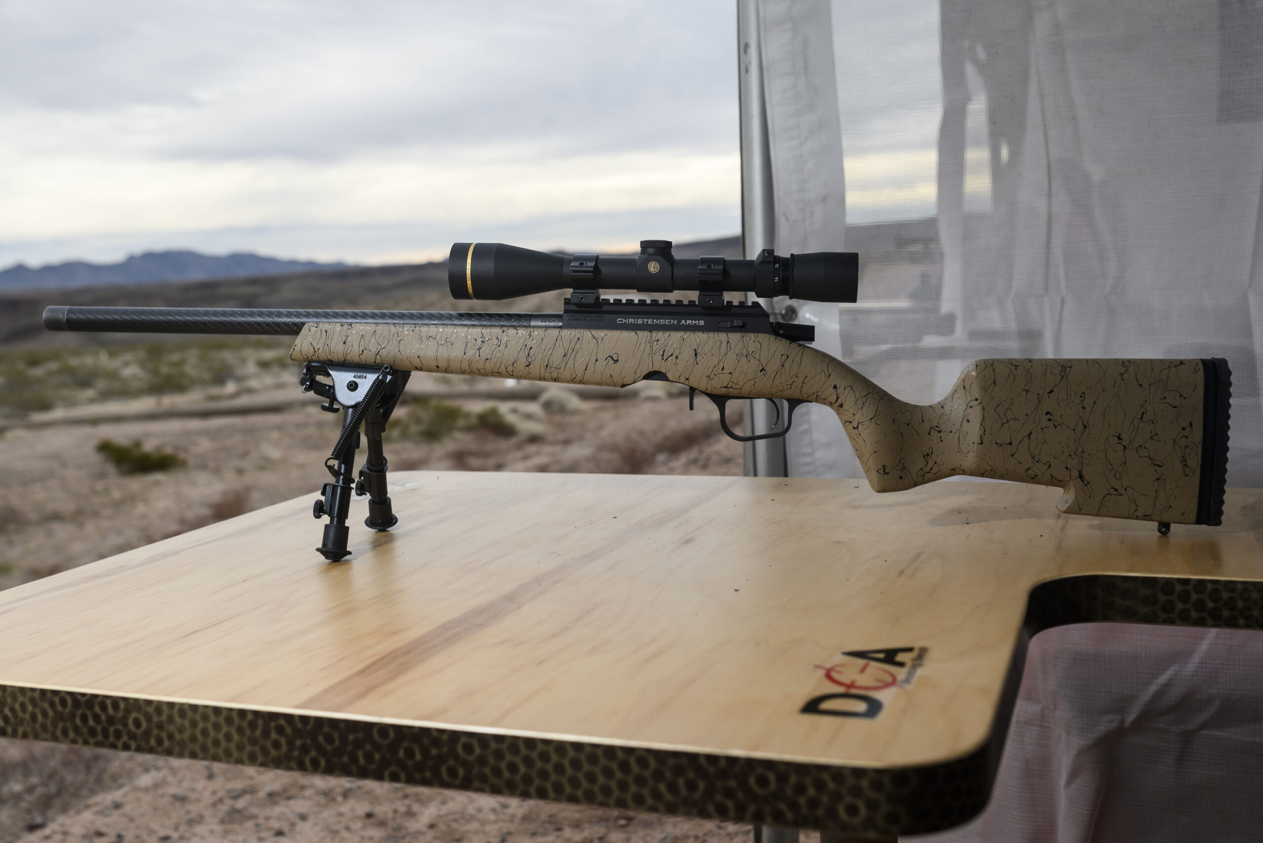 A tan Christensen Arms rimfire rifle with a scope sitting on a DOA shooting bench