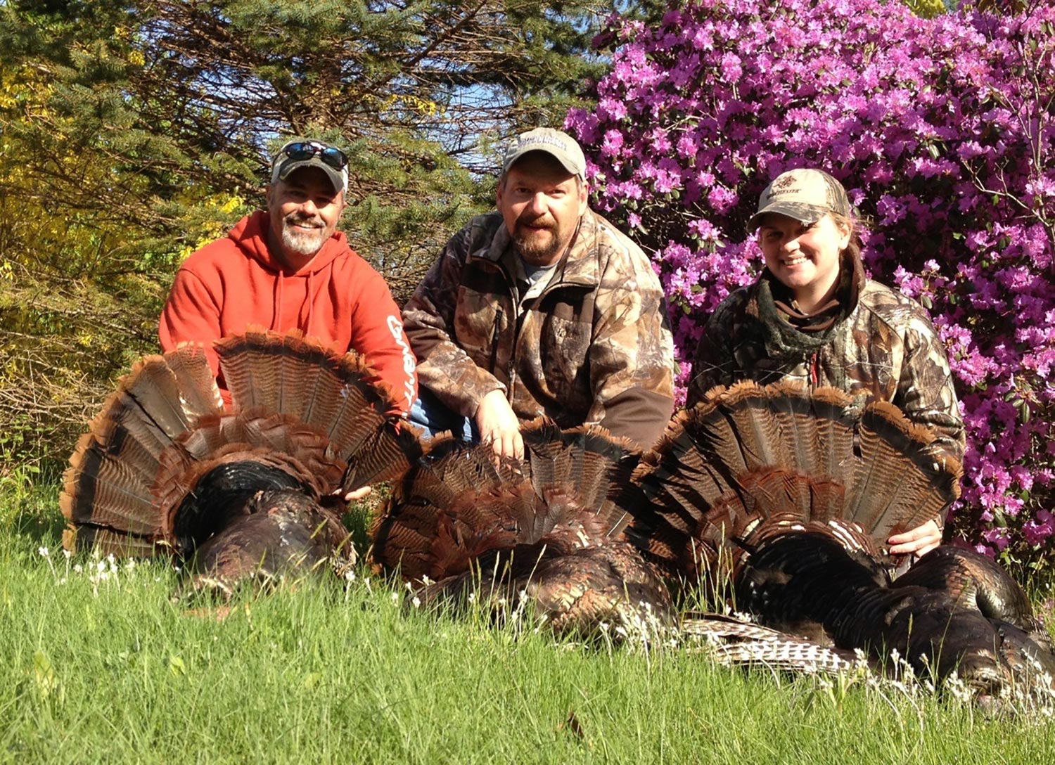 Three turkey hunters kneeling beside their turkeys.