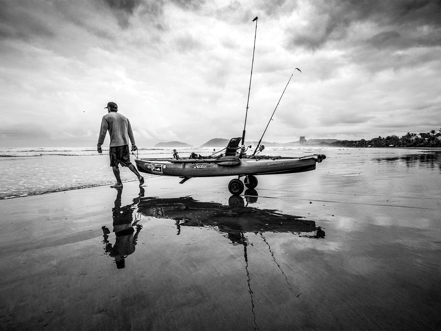 Lance Clinton carries a kayak across the beach into the surf.