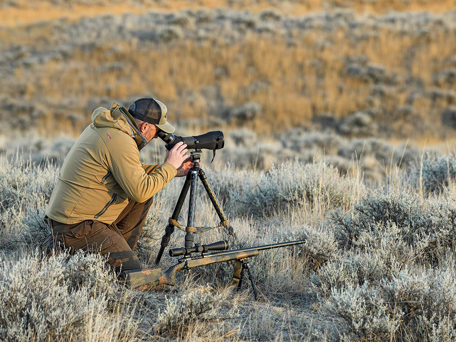 Hunter using a spotting scope in an open field.