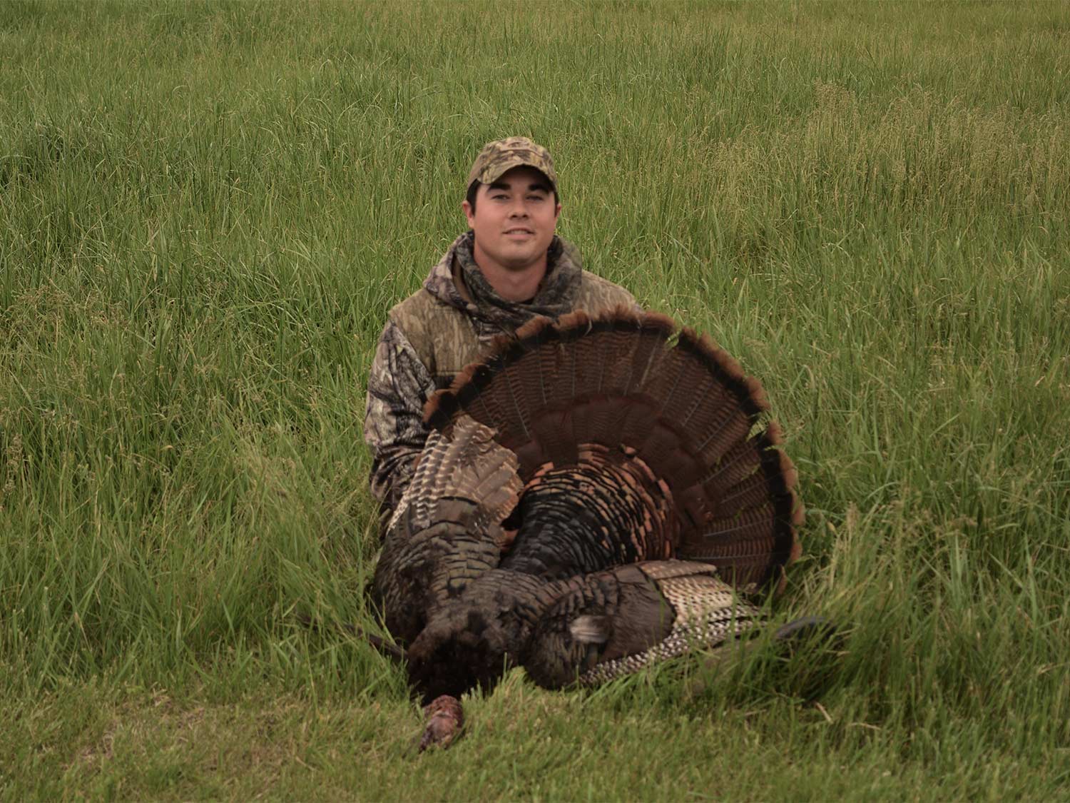 Hunter kneeling behind a turkey.