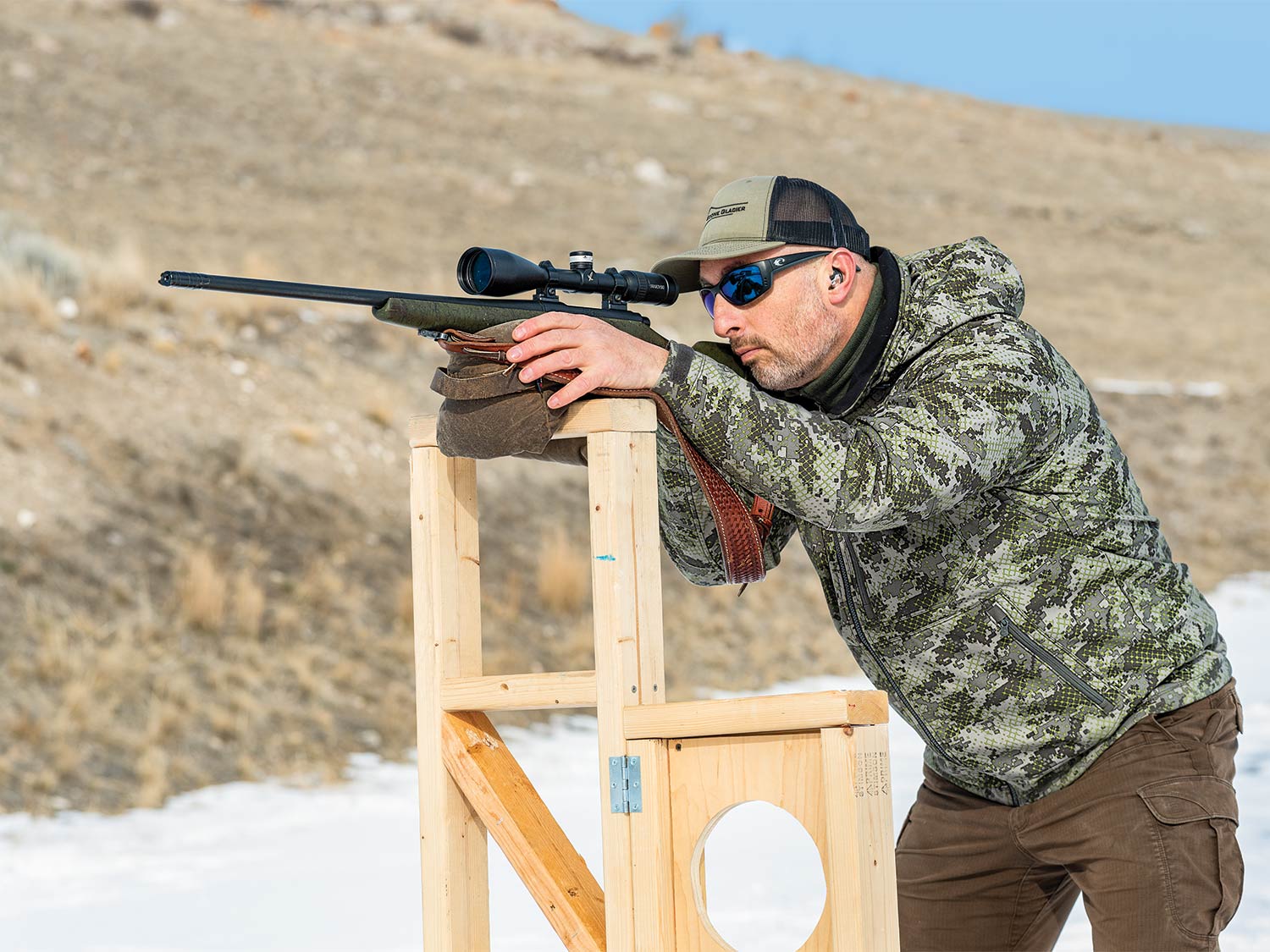 Man aiming a long-range rifle on a stand.