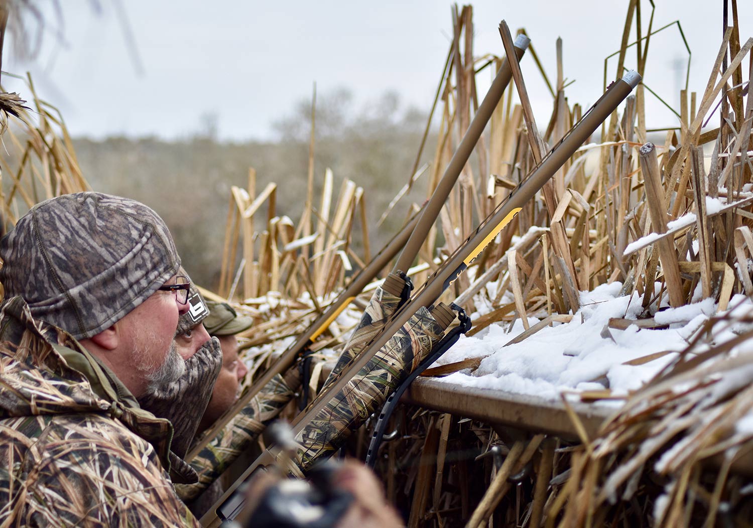 Hunter aiming shotguns in a hunting blind.
