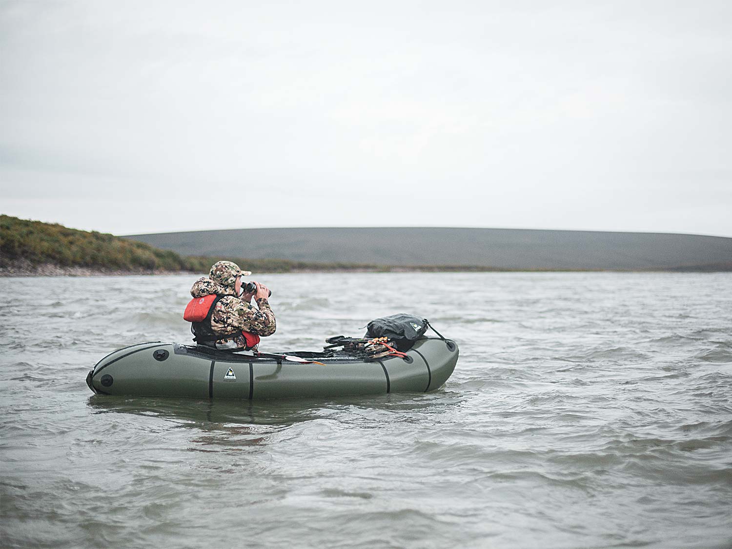 Hunter in a packraft scouting a riverbank.