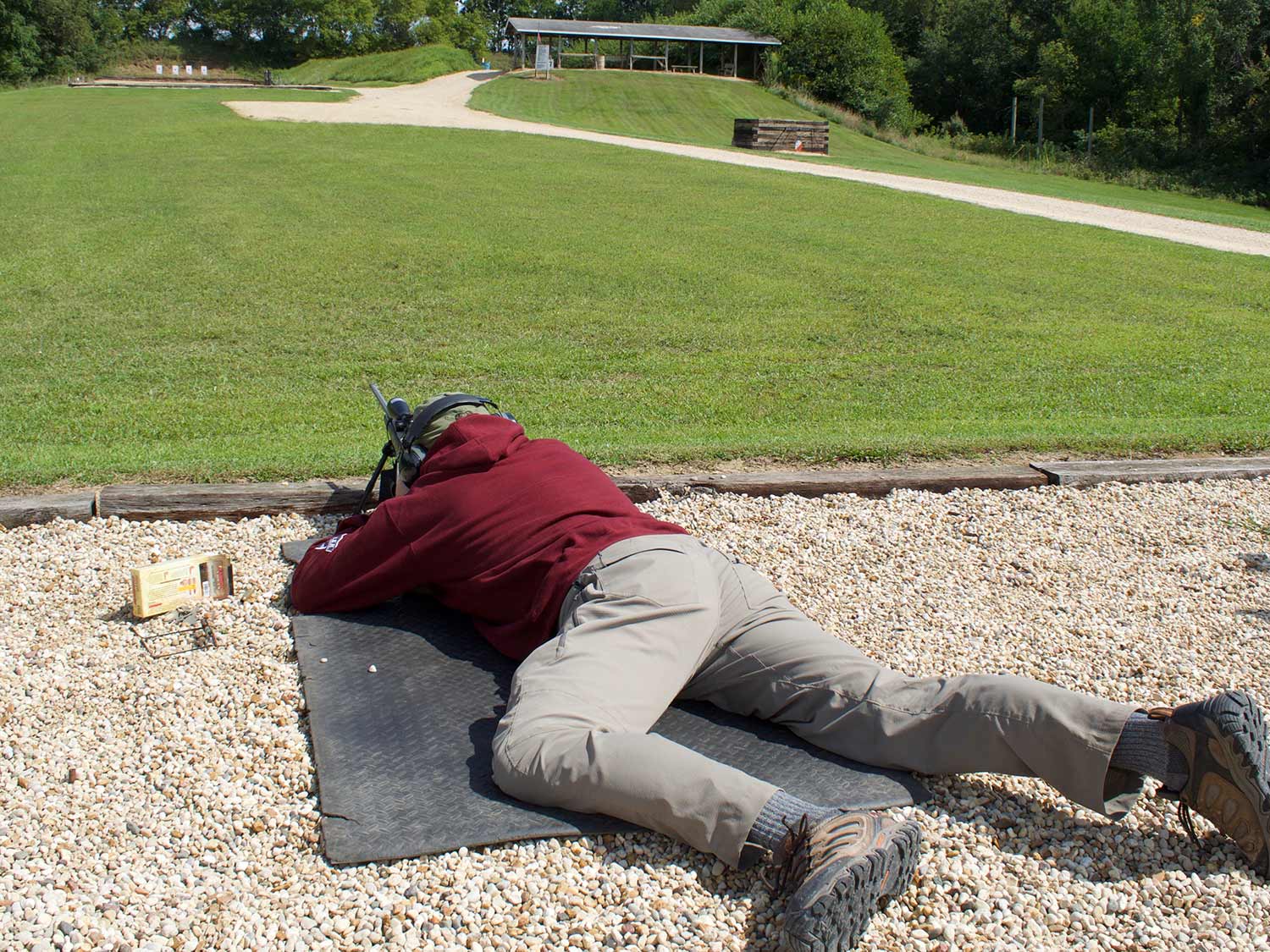 Man lying prostrate on the ground while aiming a rifle.