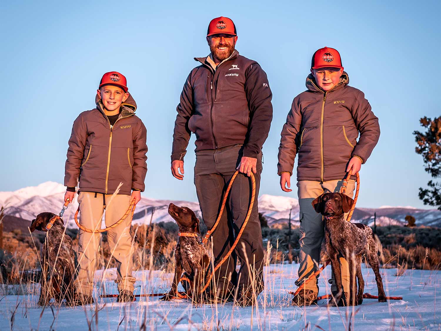A man and two young boys training hunting dogs.