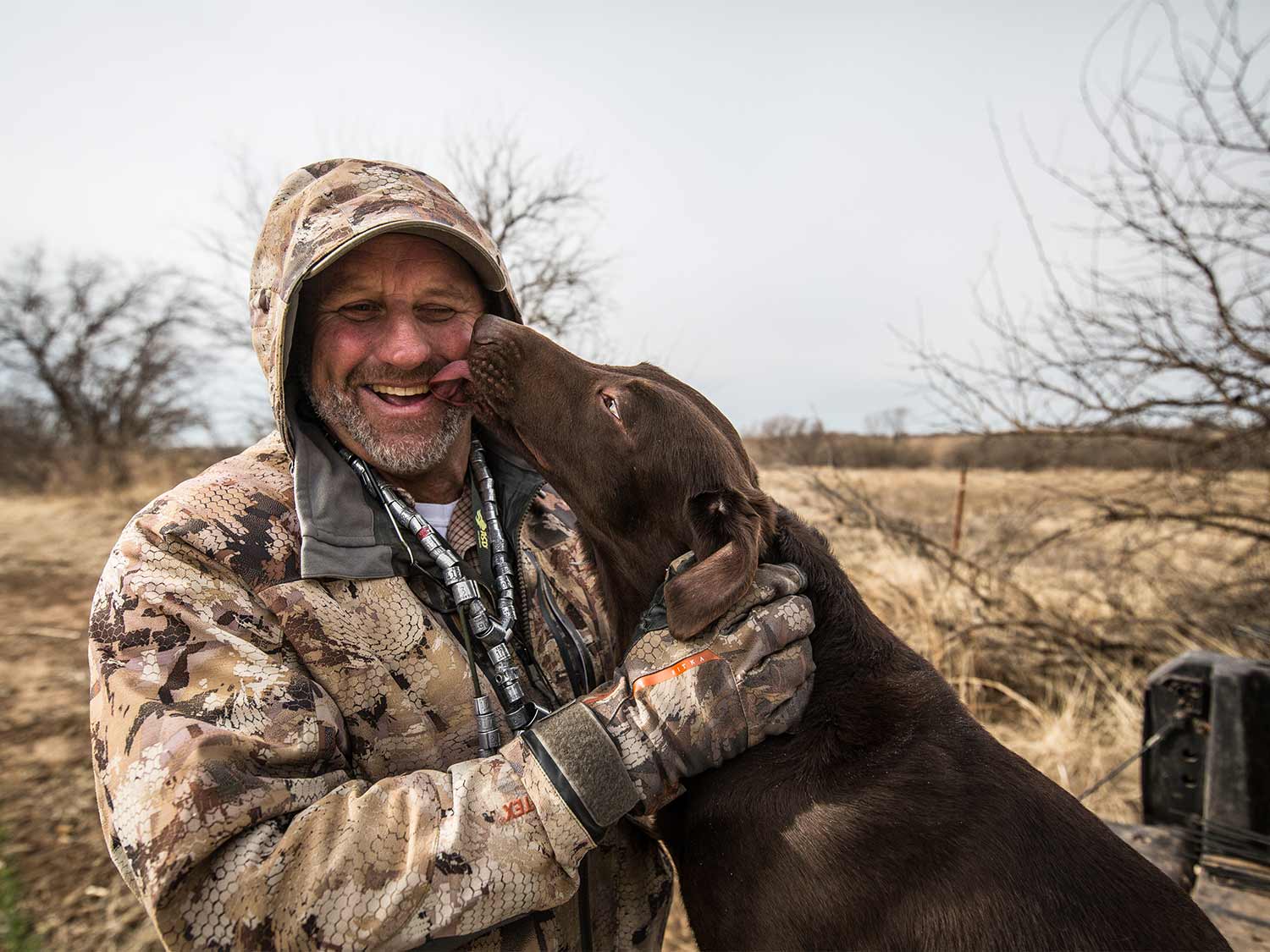 A man and a chocolate lab in a field.