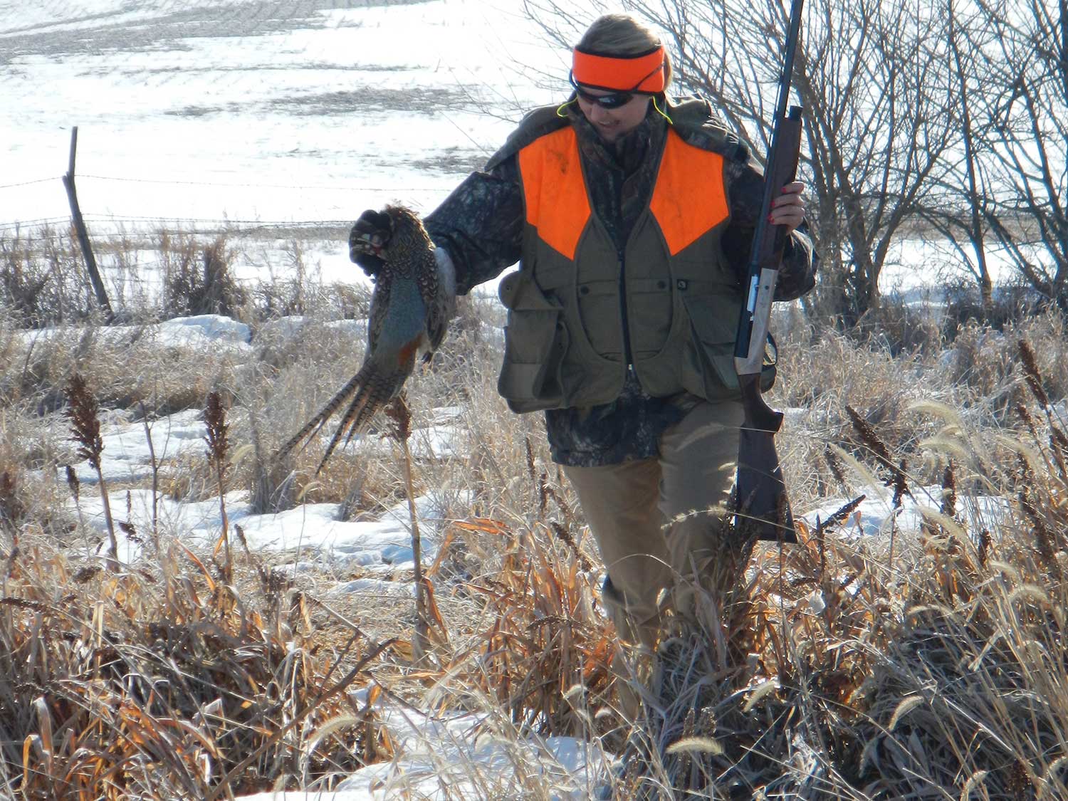 A hunter carrying a pheasant through the snow.