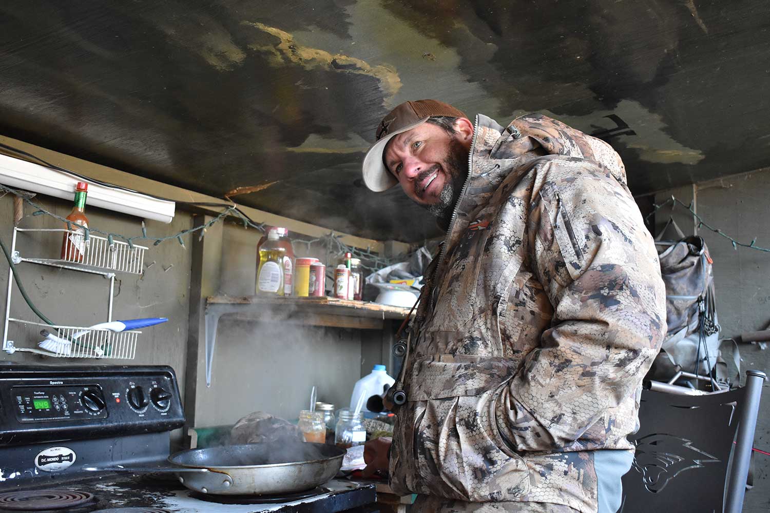 A hunter cooking breakfast inside a duck blind.