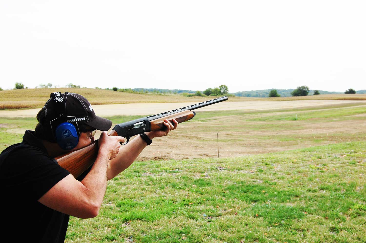 A man aiming a shotgun in an open field.