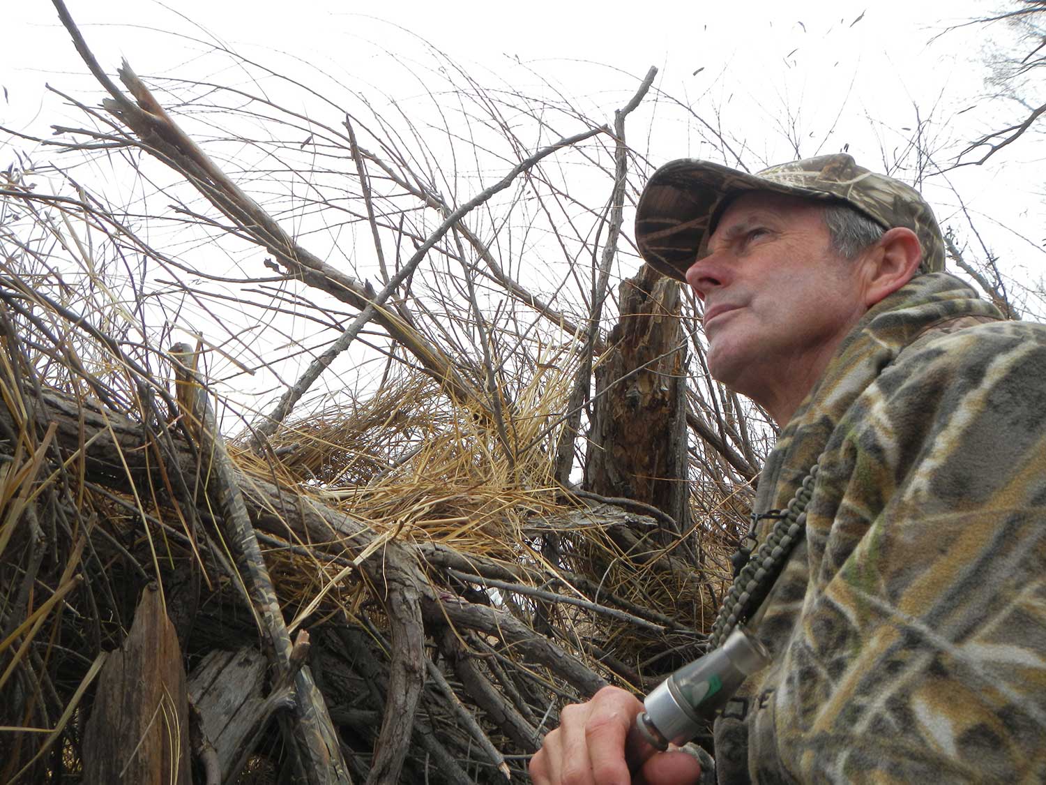 A hunter in a brush blind with a duck call.