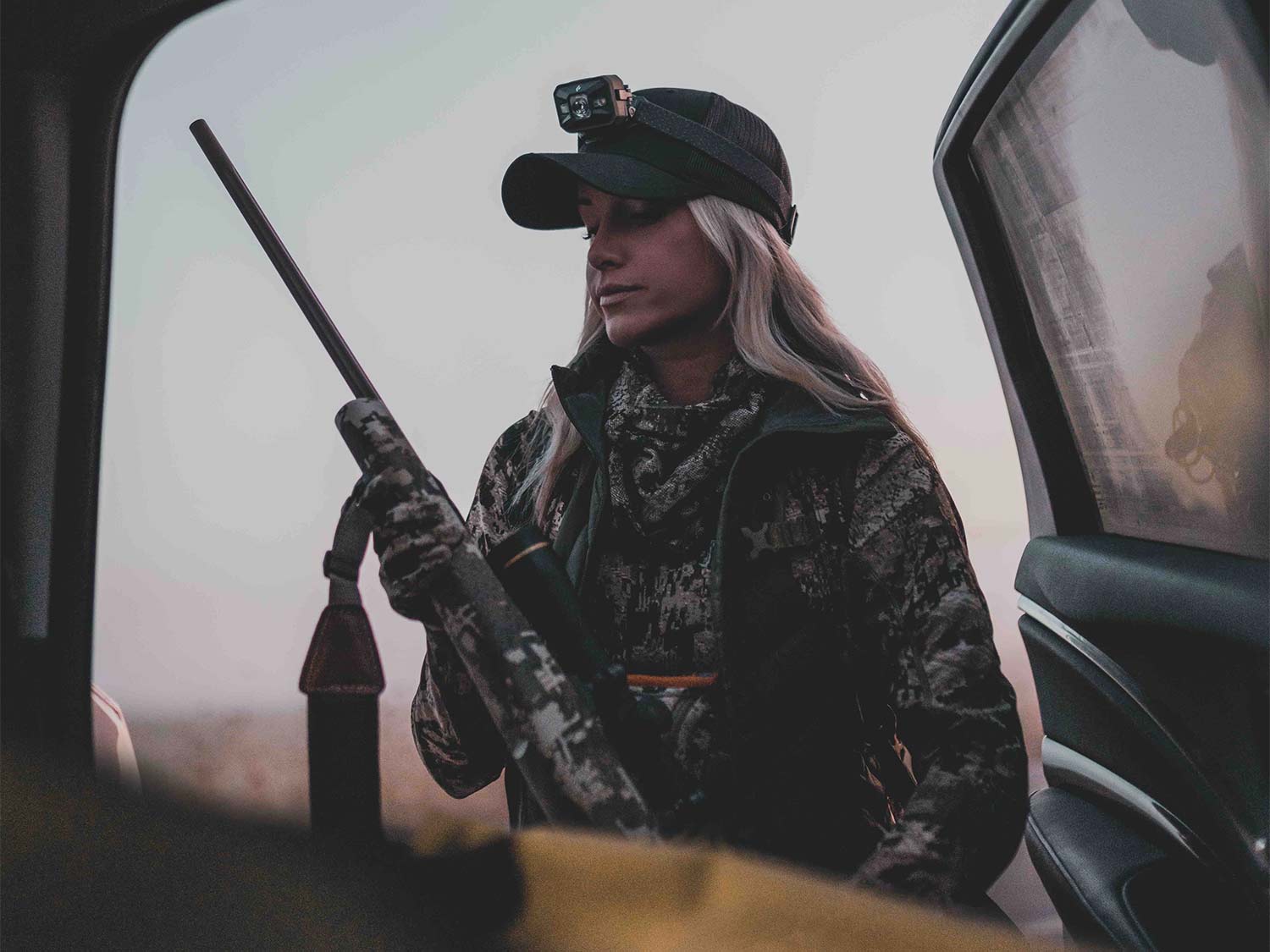 Female hunter standing beside an open truck door.