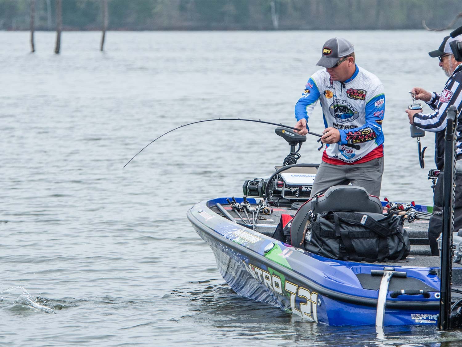An angler reels in a large bass near a boat.