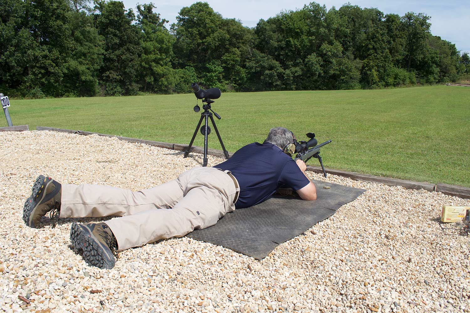 A man laying prostrate on the ground while aiming a rifle using bipods.