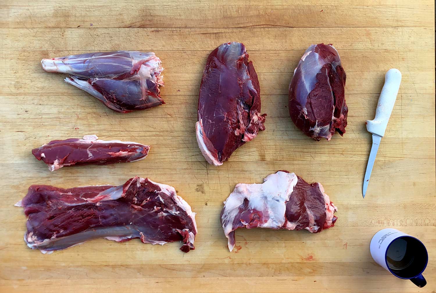 A collection of quartered and trimmed wild game meat on a wooden table.