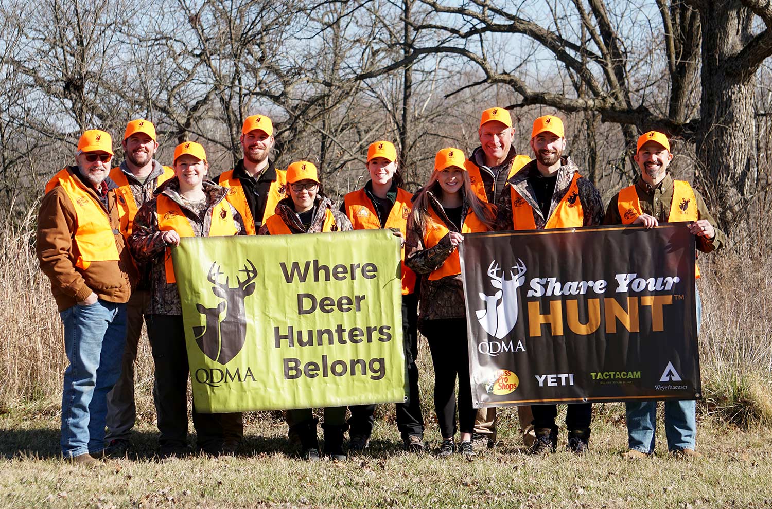 A group of hunters in orange holding up promotional signage.