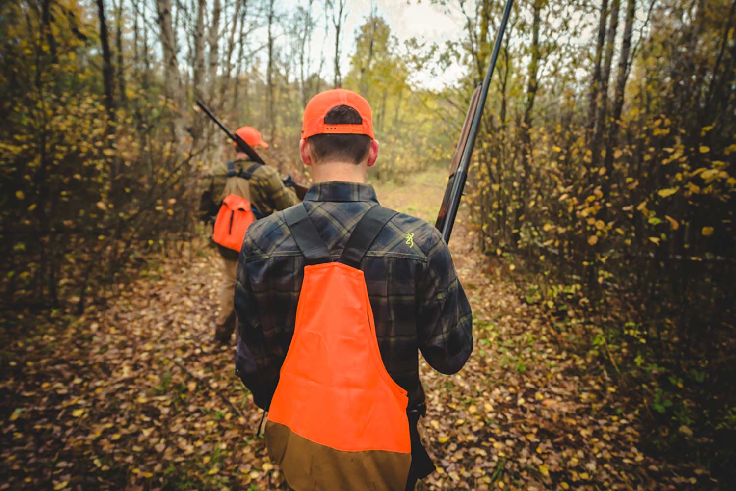 A hunter in orange walking through a trail in the woods.