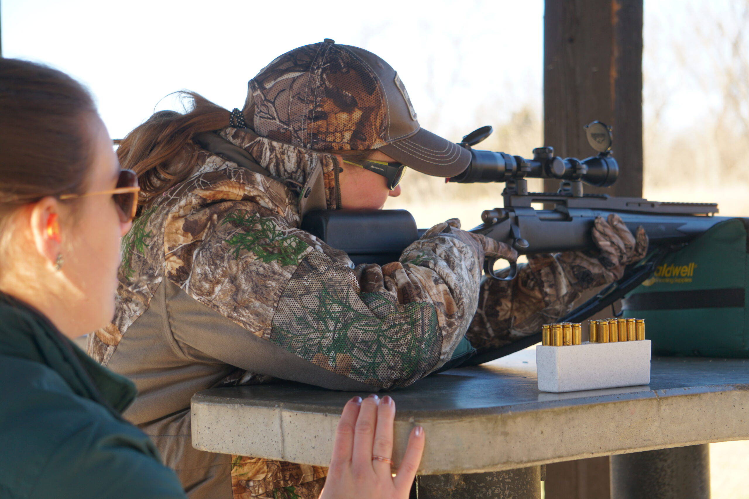 Deer hunter sights in her hunting rifle at the shooting range while an instructor watches.