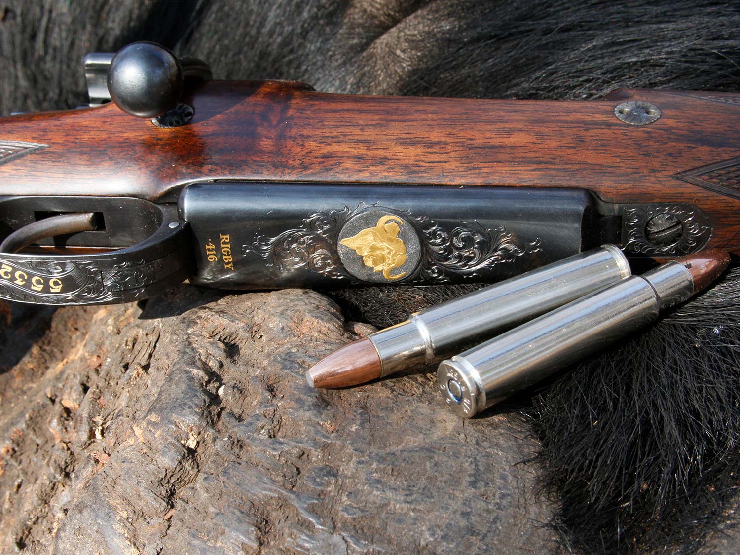 A hunting rifle and and hunting ammo cartridges on a rock.