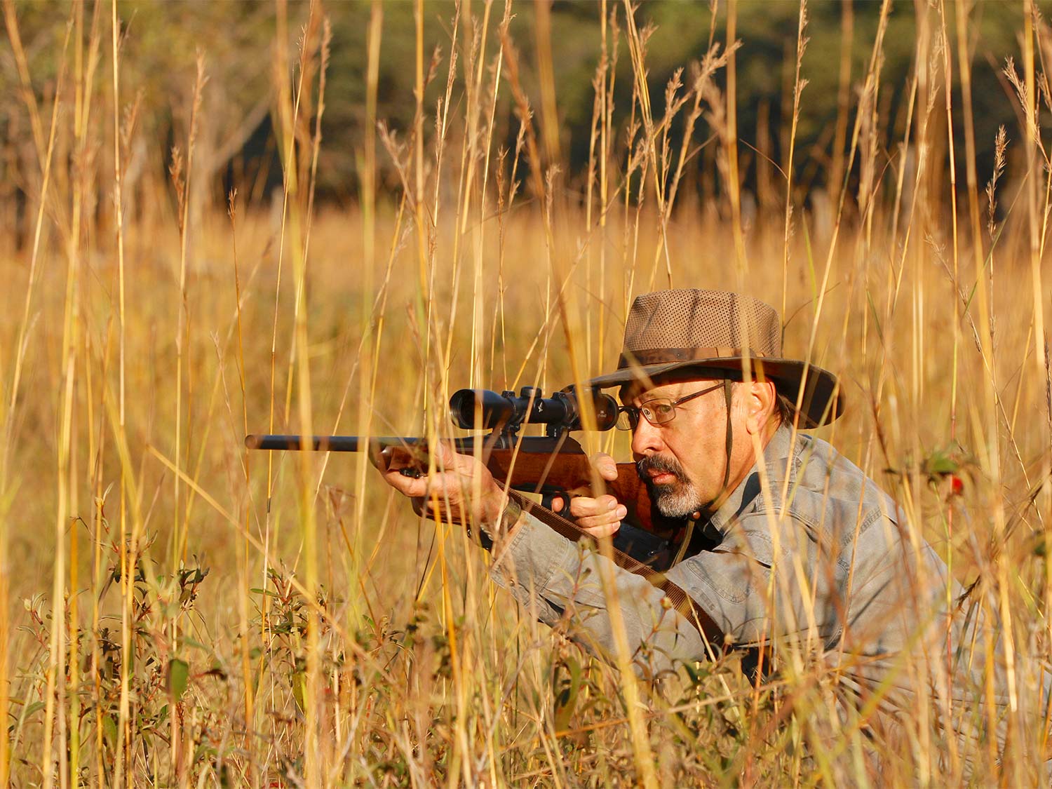 A hunter aiming a rifle in a large field while on an African Safari.