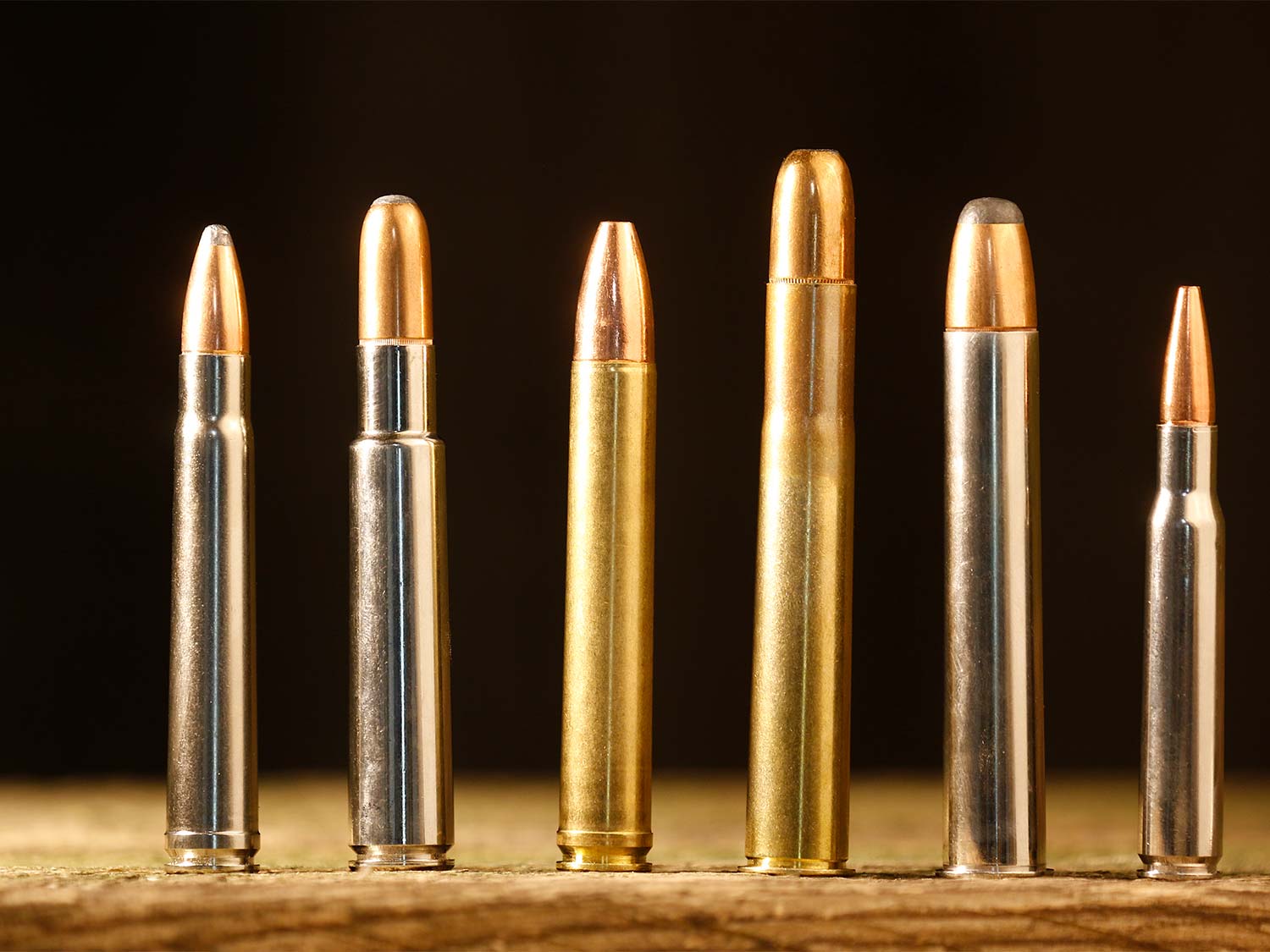 A lineup of six rifle ammo cartridges standing on a table.