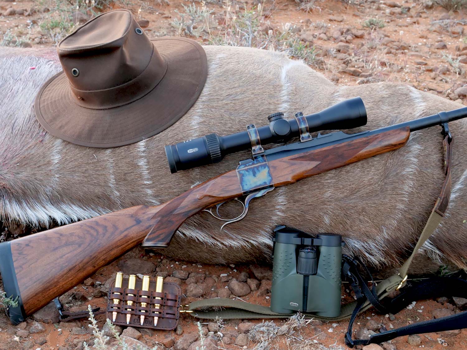 A setup of hunting rifles, ammo, and hunting gear next to down big game.