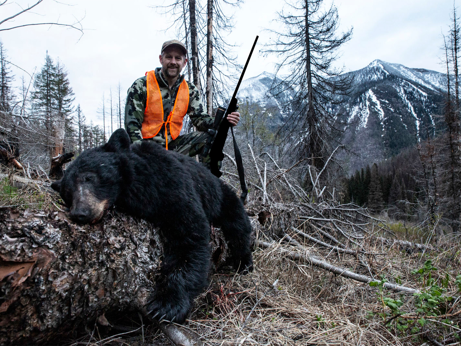 A hunter with a large black bear in the forest.