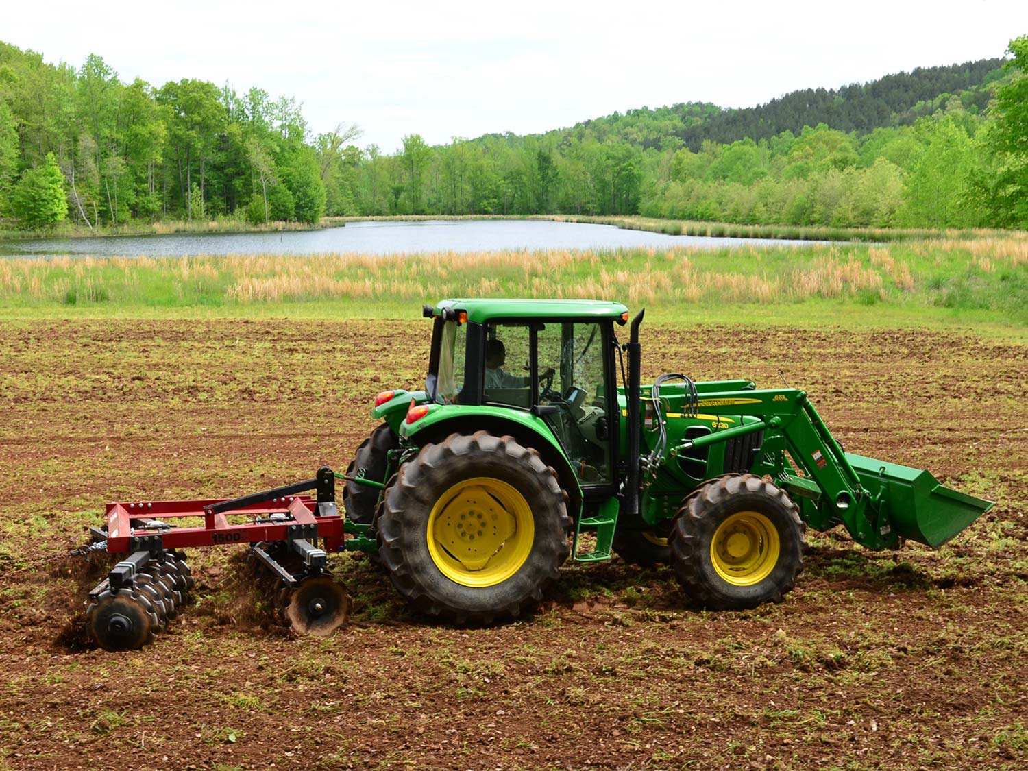 A tractor equipped with a disc tiller plows through a field.