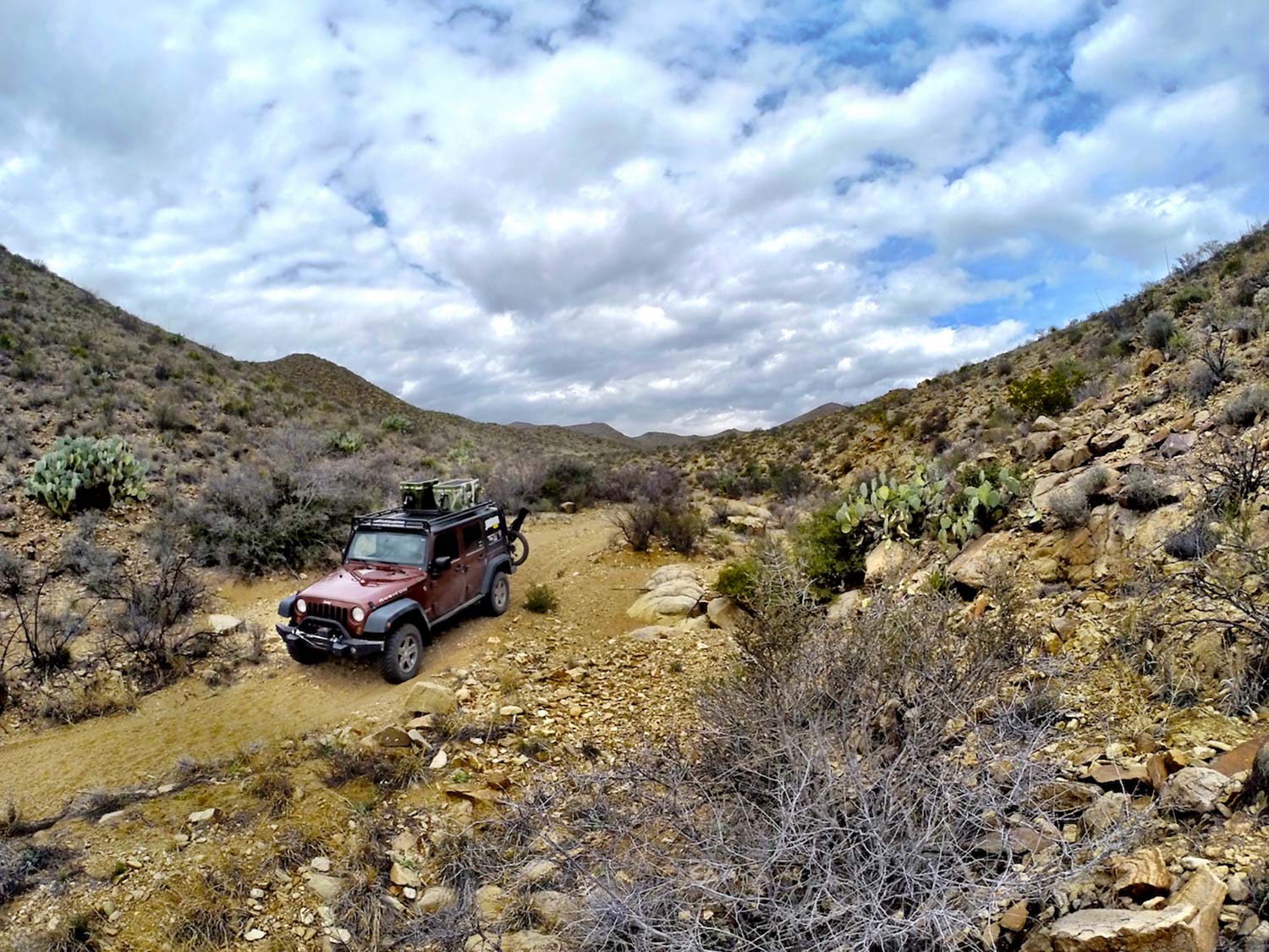 A Jeep Wrangler Rubicon in red drives through an overland hunting trail.