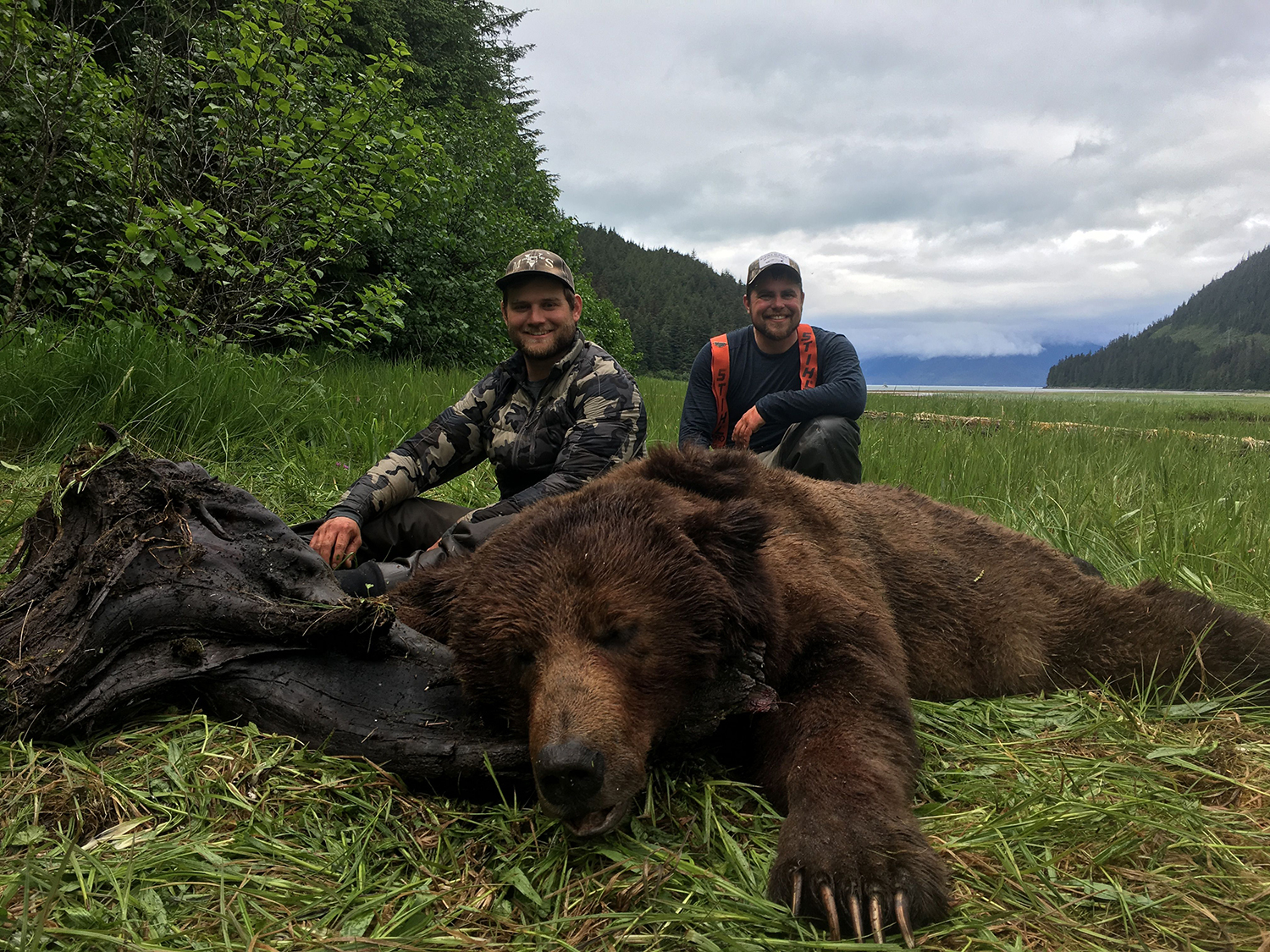 A hunter kneeling beside a large brown bear in the Tongass National Forest.