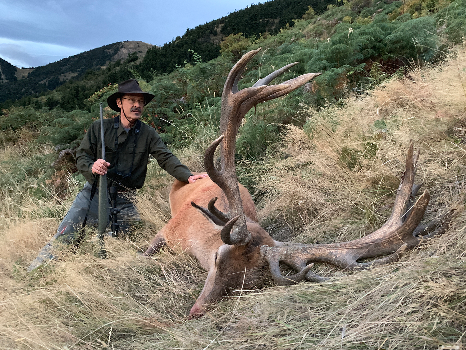 A hunter kneeling next to a large big red stag.