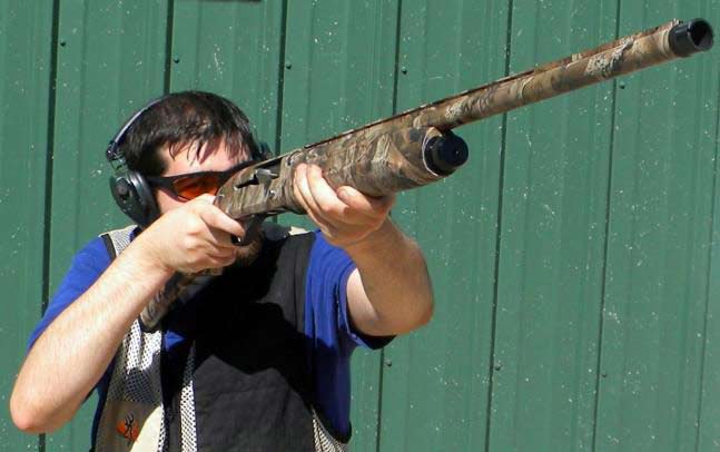 A man in shooting gear aiming a Baikal shotgun.