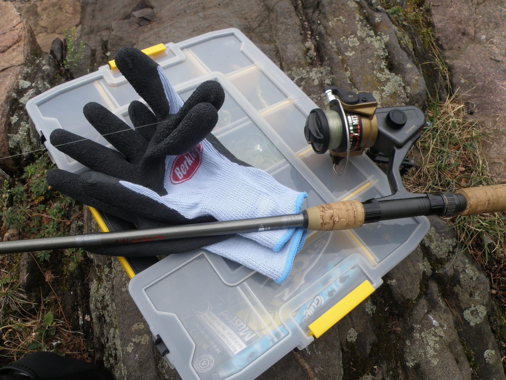 A fishing glove, rod, and reel resting on a tackle box.