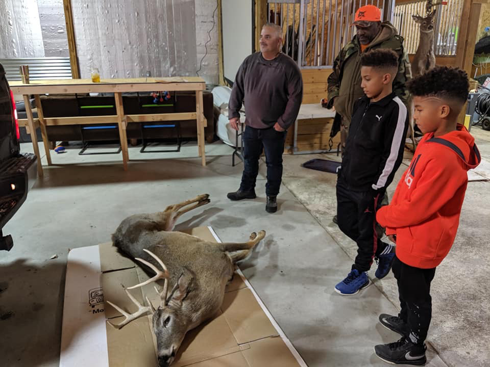 Two men and two stand overlooking a whitetail deer.