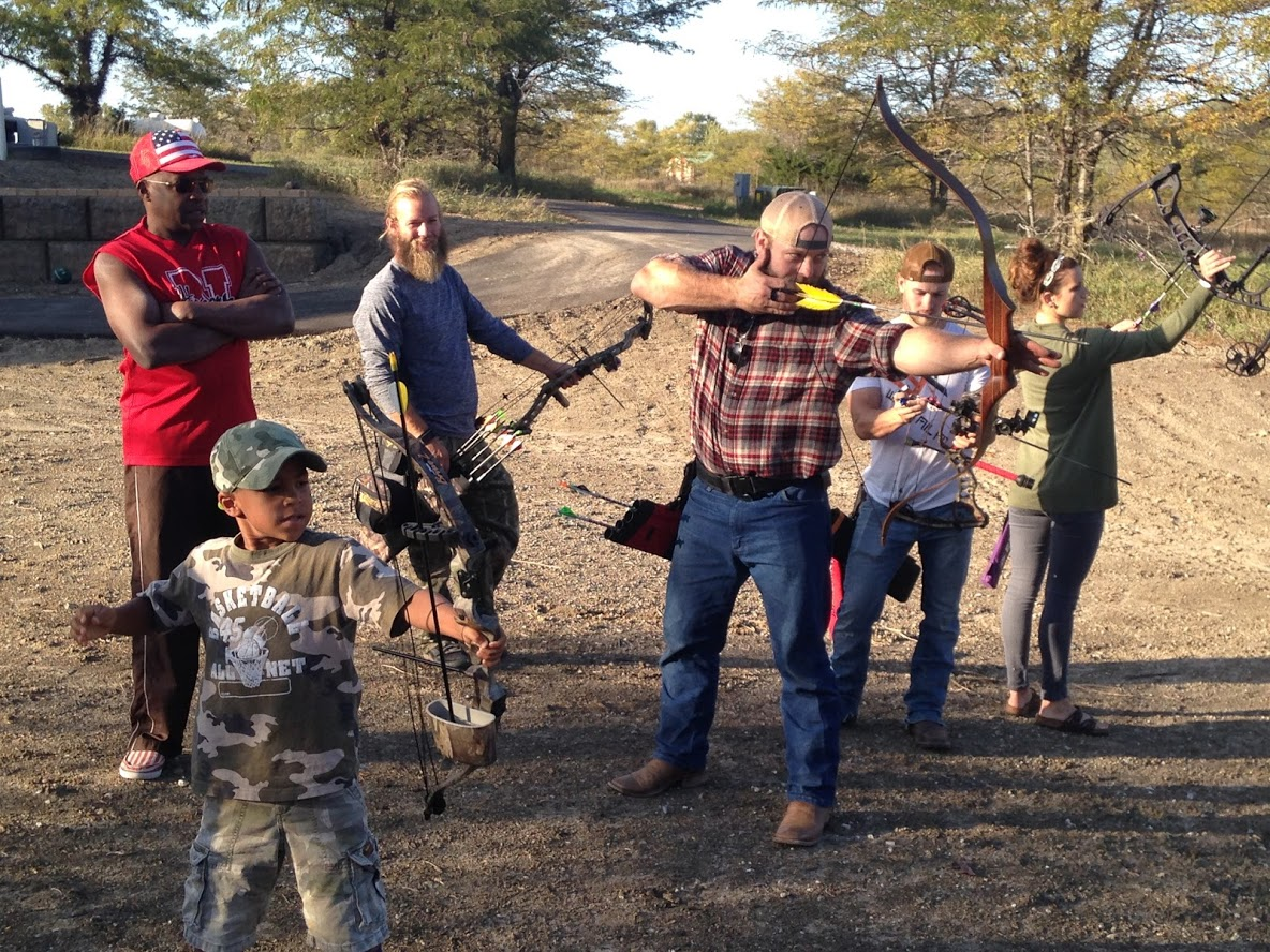 Group of bearded men and a kid shooting traditional bows for target practice
