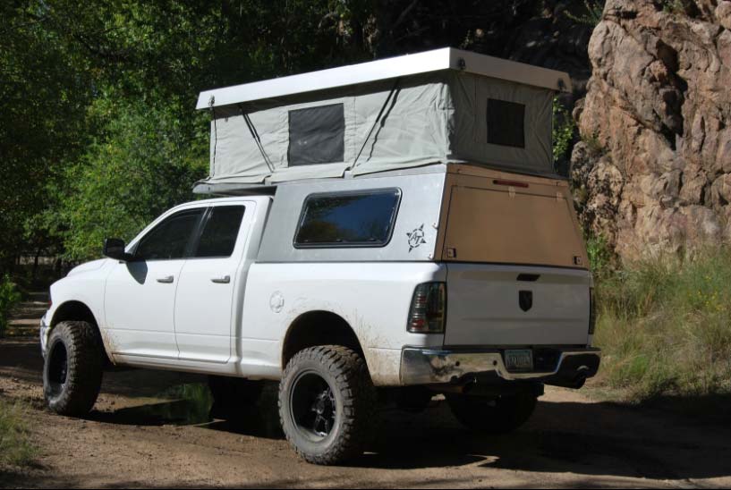 A camping tent and hard top on the bed of a white truck.