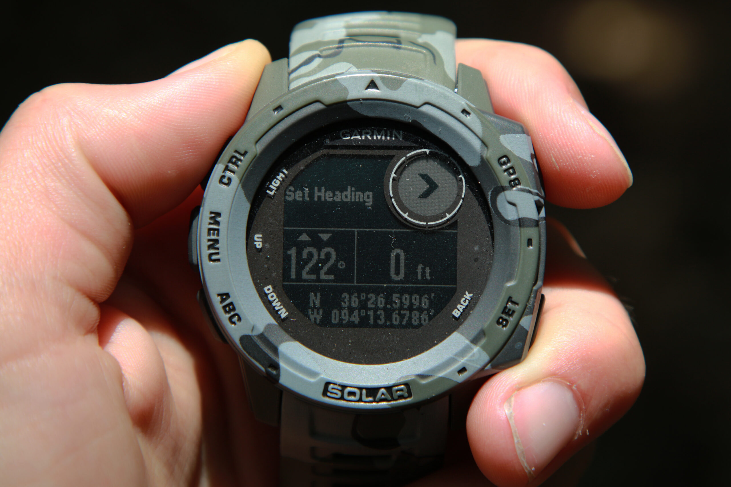A hand-held camo Garmin GPS smart watch with a display reading "set heading"