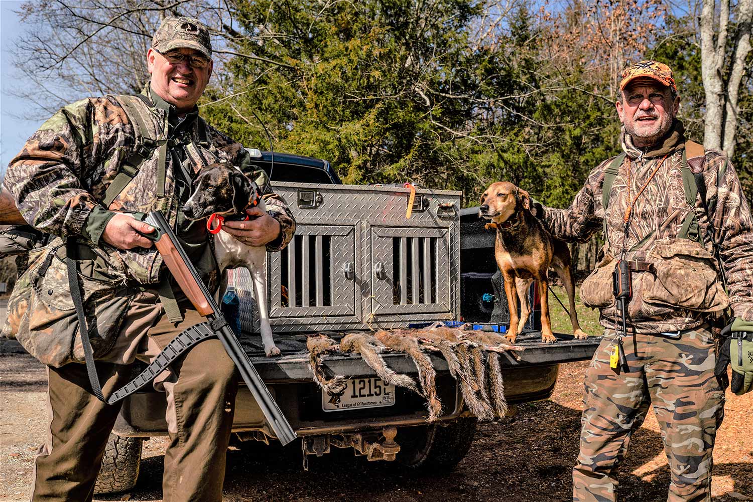 Two hunters standing next to a truck with a hunting dog on the tailgate.