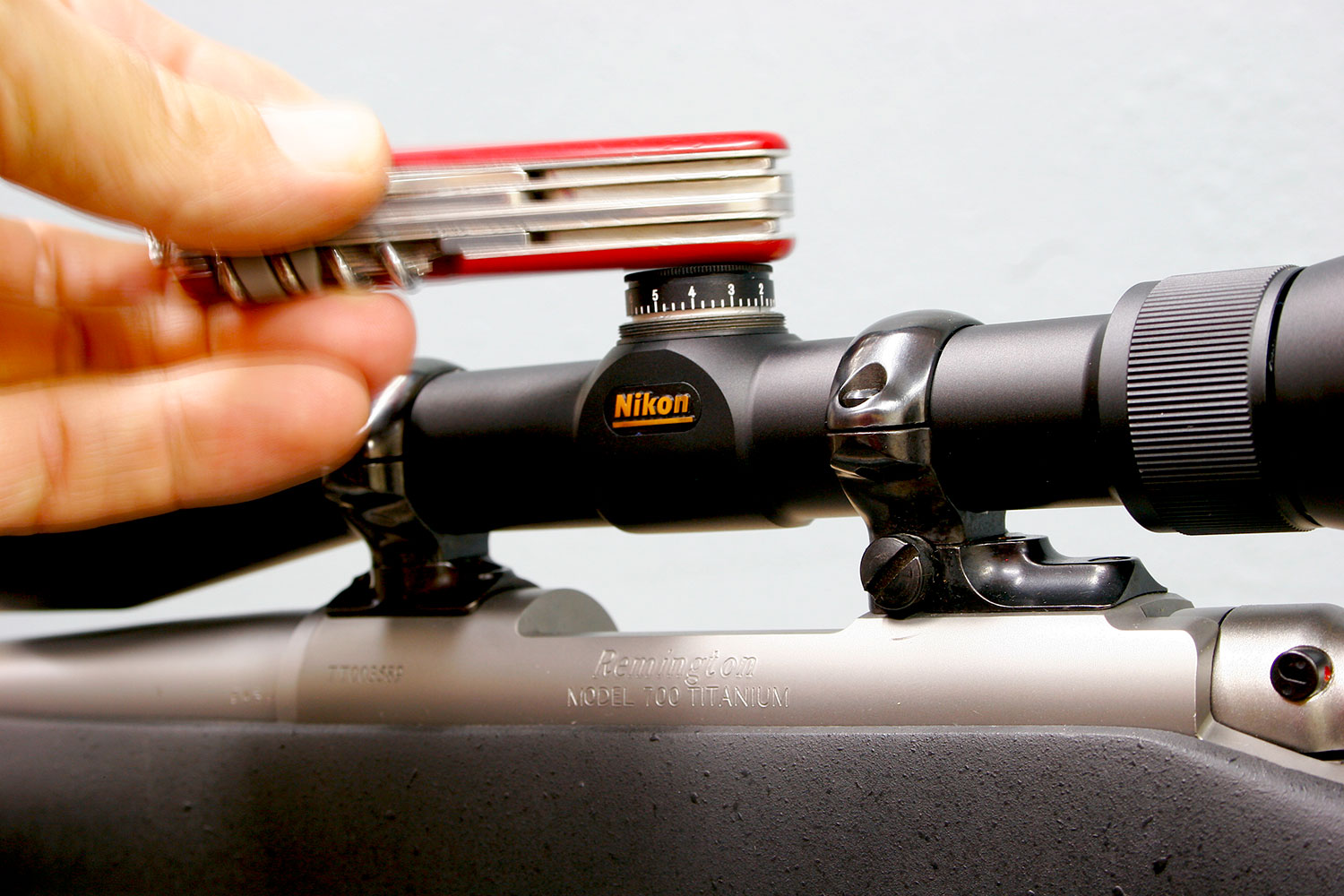 Hand using a swiss army knife on a rifle scope.